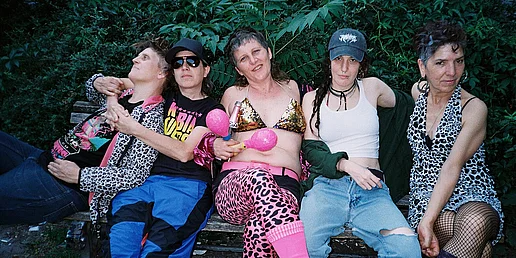 Die fünf MItglieder der Kumbia Queers sitzen auf einer Bank vor einer Palme